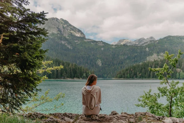 Jovem mulher na margem do lago da montanha. As costas da menina contra o fundo das montanhas. Menina sentada perto de belo Lago Negro em Montenegro. Papel de parede original de manhã de verão — Fotografia de Stock