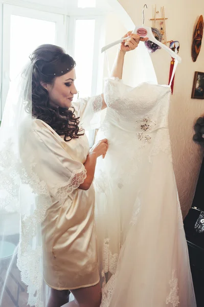 Happy beautiful bride tries on a wedding dress dressing gown. Girl have final preparation for wedding. Beautiful newlywed woman with long hair — Stock Photo, Image