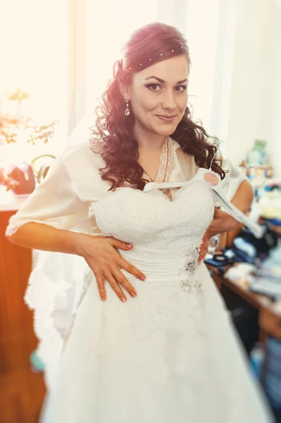 Happy beautiful bride tries on a wedding dress dressing gown. Girl have final preparation for wedding. Beautiful newlywed woman with long hair — Stock Photo, Image