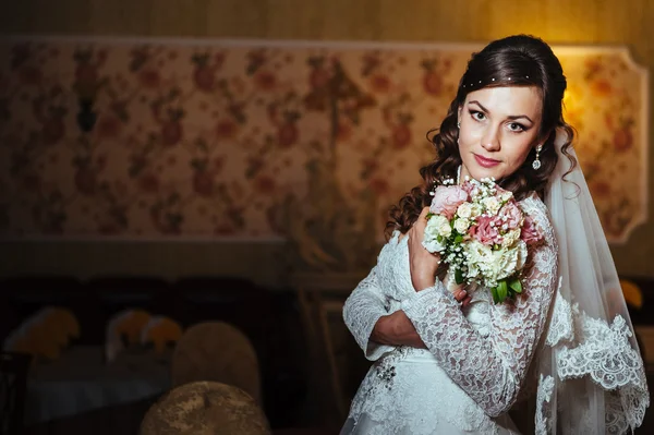 Hinreißende Braut Blondine im Hochzeitskleid auf luxuriösem Interieur mit Diamantschmuck posiert zu Hause und wartet auf Bräutigam. — Stockfoto