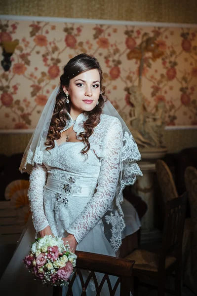 Hermosa novia rubia en vestido de novia en el interior de lujo con joyas de diamantes posando en casa y esperando al novio . — Foto de Stock