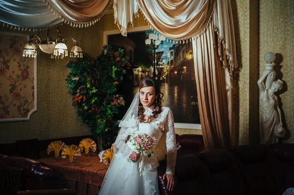 Splendida sposa bionda in abito da sposa su interni di lusso con gioielli di diamanti in posa a casa e in attesa di sposo . — Foto Stock