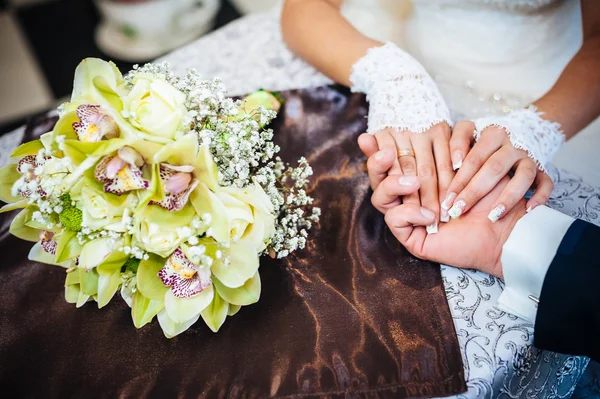 Закройте руки влюбленной пары, сидящей в кафе в день своей свадьбы. Букет цветов — стоковое фото