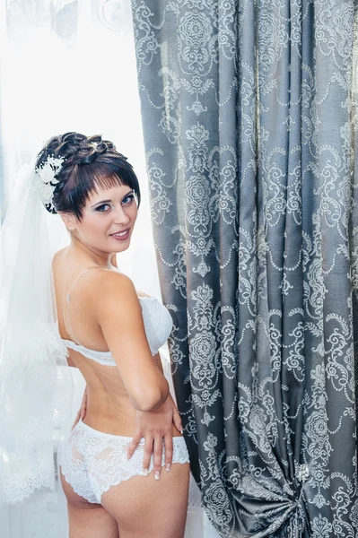 Sposa nuda Spogliarello. Bella ragazza in lingerie bianca giocare con il suo abito da sposa. Giovane donna allegra posa — Foto Stock