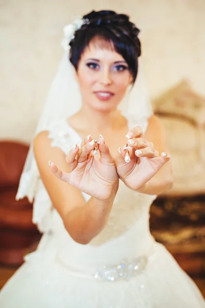 Bride holding earrings. Portrait of a gorgeous woman adjusting her earring. Preparation moment for the wedding. — Stock Photo, Image