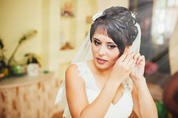 Braut mit Ohrringen. Porträt einer hinreißenden Frau, die ihren Ohrring justiert. Moment der Vorbereitung auf die Hochzeit. — Stockfoto