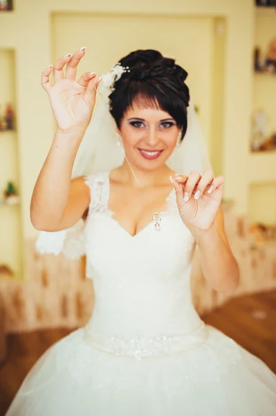 Bride holding earrings. Portrait of a gorgeous woman adjusting her earring. Preparation moment for the wedding. — Stock Photo, Image