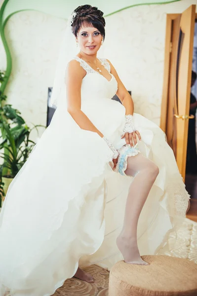 Bride putting a wedding garter on her leg — Stock Photo, Image