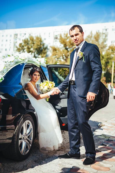 Gelukkige bruidegom zijn bruid uit de bruiloft auto helpen. — Stockfoto