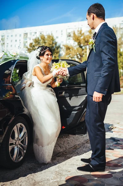Happy groom helping his bride out of the wedding car. — Stock Photo, Image