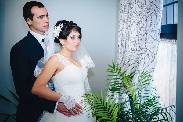 Encantadora novia con novio abraza y besos en su celebración de la boda en un restaurante de lujo. ramo de flores, vestido de novia. pareja recién casada enlujo moderno hotel hall —  Fotos de Stock