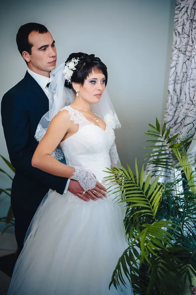 Charming bride with groom embraces and kisses on their wedding celebration in luxurious restaurant. bouquet of flowers, bridal dress. newly married couple atluxury modern hotel hall — Stock Photo, Image