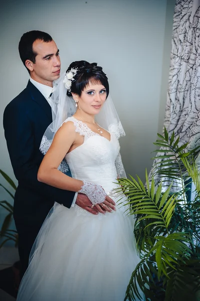 Charming bride with groom embraces and kisses on their wedding celebration in luxurious restaurant. bouquet of flowers, bridal dress. newly married couple atluxury modern hotel hall — Stock Photo, Image