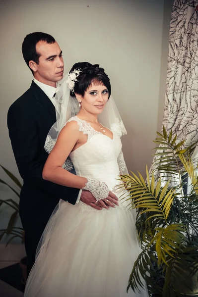 Charmig brud med brudgummen omfamnar och kysser på deras bröllop fest i lyxig restaurang. bukett av blommor, brudklänning. Nyligen gift par atluxury moderna hotell hall — Stockfoto