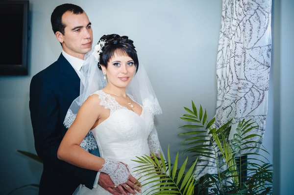 Charming bride with groom embraces and kisses on their wedding celebration in luxurious restaurant. bouquet of flowers, bridal dress. newly married couple atluxury modern hotel hall — Stock Photo, Image