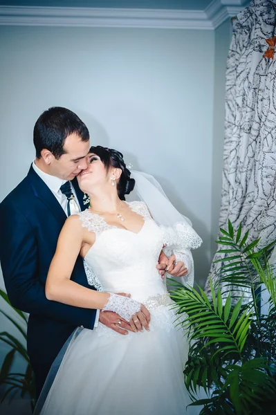 Charming bride with groom embraces and kisses on their wedding celebration in luxurious restaurant. bouquet of flowers, bridal dress. newly married couple atluxury modern hotel hall — Stock Photo, Image