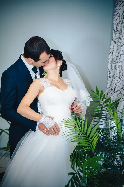 Charming bride with groom embraces and kisses on their wedding celebration in luxurious restaurant. bouquet of flowers, bridal dress. newly married couple atluxury modern hotel hall — Stock Photo, Image