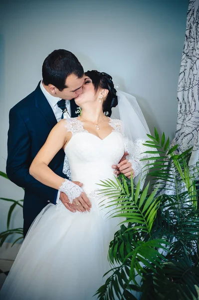 Encantadora novia con novio abraza y besos en su celebración de la boda en un restaurante de lujo. ramo de flores, vestido de novia. pareja recién casada enlujo moderno hotel hall — Foto de Stock