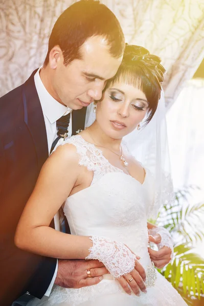 Charming bride with groom embraces and kisses on their wedding celebration in luxurious restaurant. bouquet of flowers, bridal dress. newly married couple atluxury modern hotel hall — Stock Photo, Image