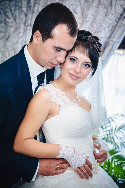 Очаровательная невеста с женихом обнимает и целует на их свадьбе в роскошном ресторане. букет цветов, свадебное платье. молодожёны в роскошном современном гостиничном зале — стоковое фото