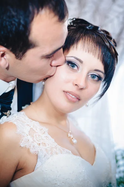 Encantadora novia con novio abraza y besos en su celebración de la boda en un restaurante de lujo. ramo de flores, vestido de novia. pareja recién casada enlujo moderno hotel hall — Foto de Stock