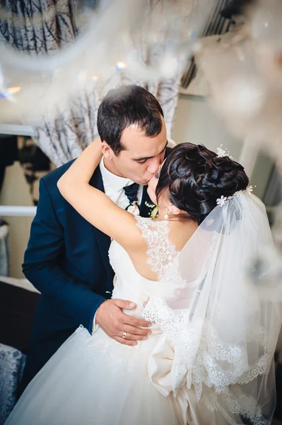 Charming bride with groom embraces and kisses on their wedding celebration in luxurious restaurant. bouquet of flowers, bridal dress. newly married couple atluxury modern hotel hall — Stock Photo, Image