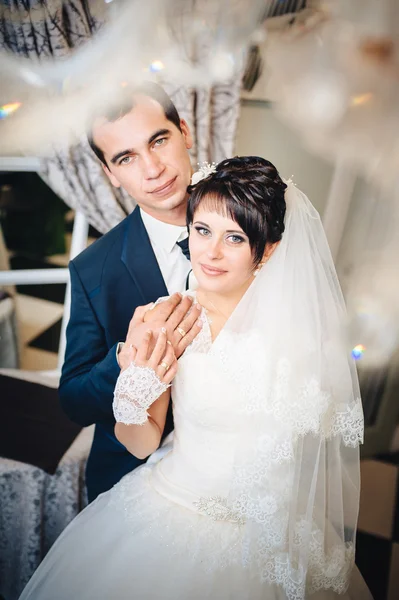 Charming bride with groom embraces and kisses on their wedding celebration in luxurious restaurant. bouquet of flowers, bridal dress. newly married couple atluxury modern hotel hall — Stock Photo, Image