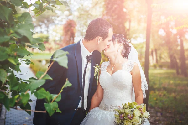 Pareja joven besándose en vestido de novia. Novia sosteniendo ramo de flores — Foto de Stock