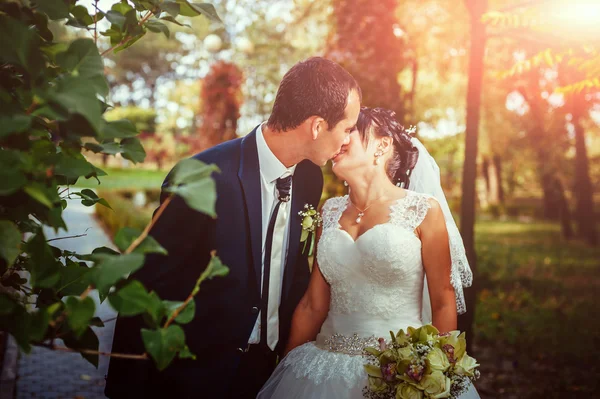 Casal jovem beijando no vestido de casamento. Noiva segurando buquê de flores — Fotografia de Stock