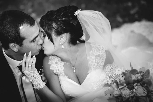 Casal jovem beijando no vestido de casamento. Noiva segurando buquê de flores — Fotografia de Stock