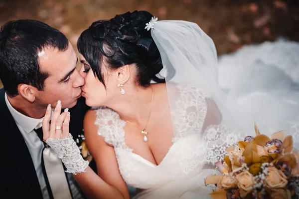 Pareja joven besándose en vestido de novia. Novia sosteniendo ramo de flores —  Fotos de Stock