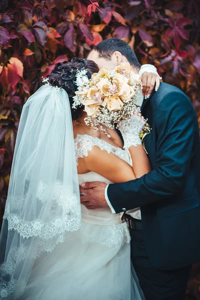 Young couple kissing in wedding gown. Bride holding bouquet of flowers — Stock Photo, Image