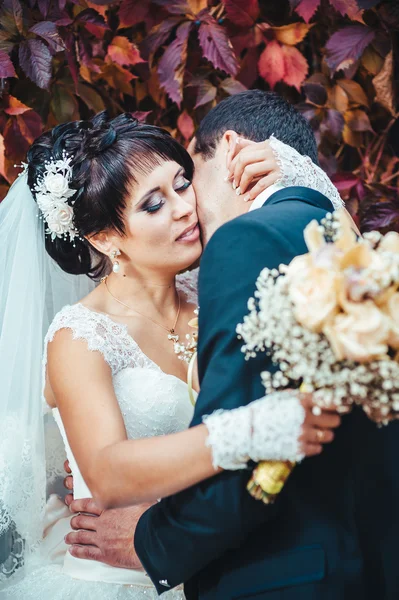 Young couple kissing in wedding gown. Bride holding bouquet of flowers — Stock Photo, Image