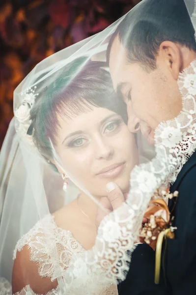 Pareja joven besándose en vestido de novia. Novia sosteniendo ramo de flores — Foto de Stock