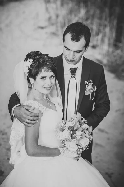 Giovane coppia che si bacia in abito da sposa. Sposa che tiene mazzo di fiori — Foto Stock