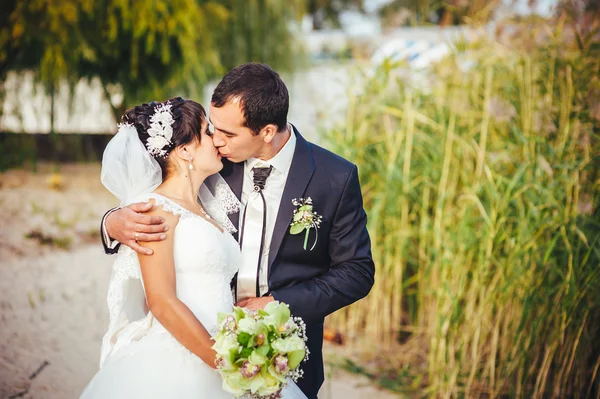 Pareja joven besándose en vestido de novia. Novia sosteniendo ramo de flores —  Fotos de Stock