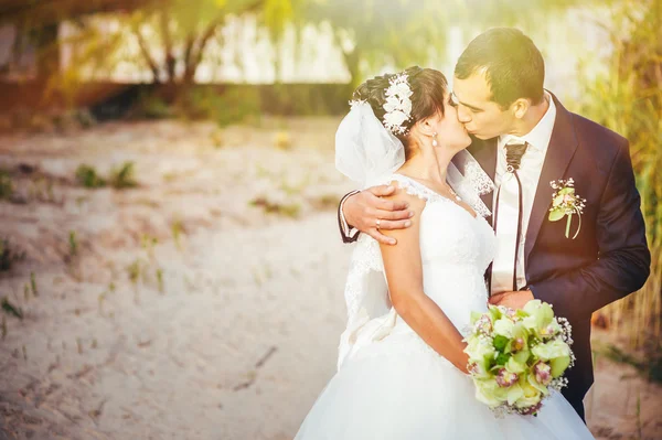 接吻的结婚礼服的年轻夫妇。新娘控股束鲜花 — 图库照片