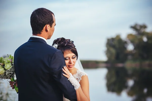 Young couple kissing in wedding gown. Bride holding bouquet of flowers — Stock Photo, Image