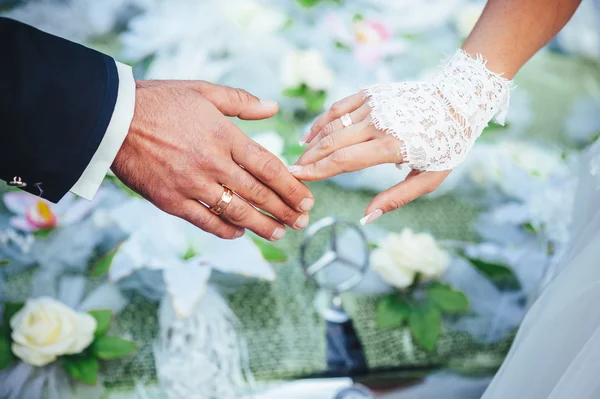 Händerna på bruden och brudgummen. bröllop bukett på svart bil — Stockfoto