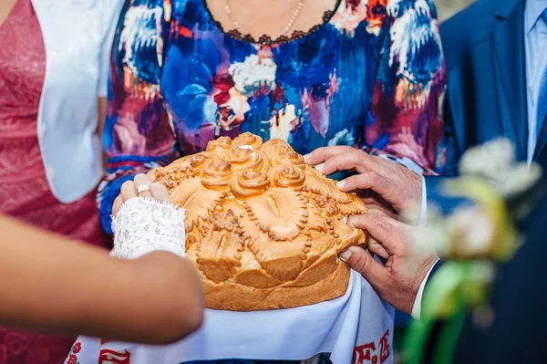 Groom holding slice of traditional wedding round loaf and bride salt it. — Stock Photo, Image