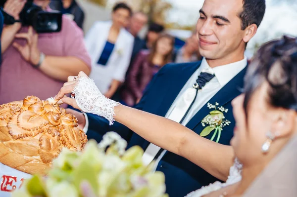 Groom holding slice of traditional wedding round loaf and bride salt it. — Stock Photo, Image