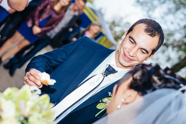 Groom holding slice of traditional wedding round loaf and bride salt it. — Stock Photo, Image