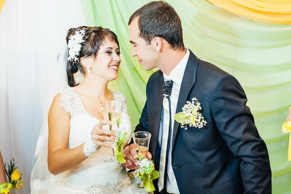 Charming bride with groom embraces and kisses on their wedding celebration in luxurious restaurant. bouquet of flowers, bridal dress. newly married couple atluxury modern hotel hall — Stock Photo, Image