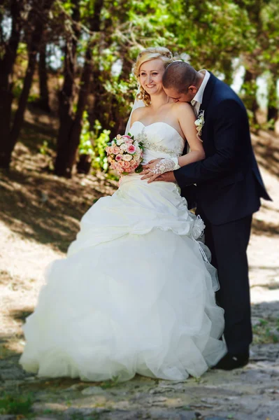 Novia y novio en el día de la boda caminando al aire libre en la naturaleza de primavera. Pareja nupcial, feliz mujer recién casada y hombre abrazándose en el parque verde. Amar pareja de boda al aire libre . — Foto de Stock