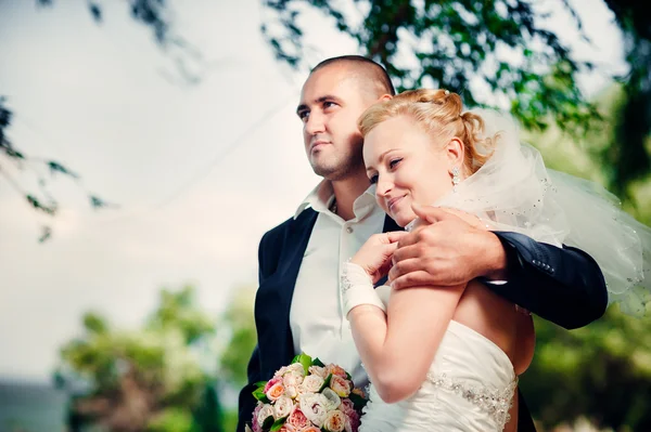 Novia y novio en el día de la boda caminando al aire libre en la naturaleza de primavera. Pareja nupcial, feliz mujer recién casada y hombre abrazándose en el parque verde. Amar pareja de boda al aire libre . — Foto de Stock