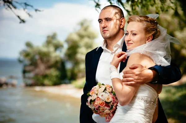 Noiva e noivo no dia do casamento andando ao ar livre na natureza de primavera. Casal nupcial, mulher recém-casada feliz e homem abraçando no parque verde. Casal de amor ao ar livre . — Fotografia de Stock