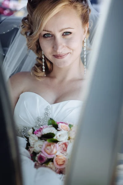 Portret van een mooie bruid in een auto. Close-up portret van een vrij verlegen bruid in een auto-venster. — Stockfoto