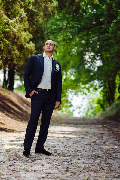 Brudgummen porträtt på en park på en bröllopsdag. Glad ung kille på deras bröllopsdag. Stilig kaukasiska man i smoking — Stockfoto