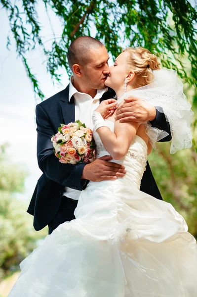 Noiva com noivo no dia do casamento andando ao ar livre na natureza de primavera. Casal nupcial, feliz mulher recém-casada e homem abraçando no parque verde . — Fotografia de Stock