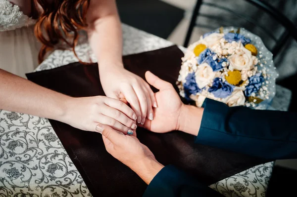 Retrato de primer plano del novio sosteniendo a las novias mano sobre la mesa cerca del ramo — Foto de Stock